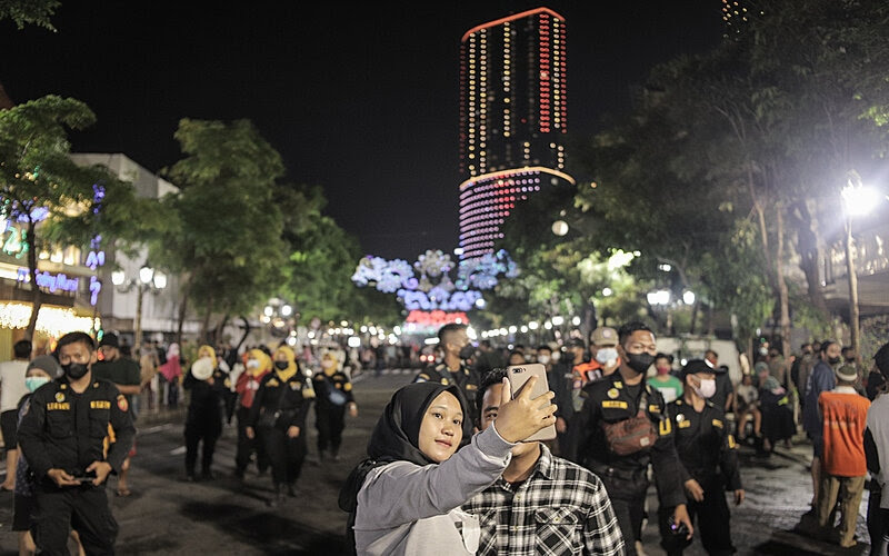 Warga melakukan swafoto sebelum petugas mengosongkan Jalan Tunjungan saat malam pergantian Tahun Baru 2022 di Surabaya, Jawa Timur, Jumat (31/12/2021). (Foto: Antara-Rizal Hanafi)