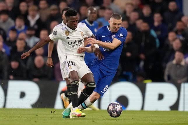 Duel antara penyerang sayap Real Madrid, Vinicius Junior dengan gelandang Chelsea, Mateo Kovacic pada laga leg kedua perempat final Liga Champions 2022/2023, Rabu (19/4/2023) WIB. (Foto: AP Photo/Kirsty Wiggleswroth)